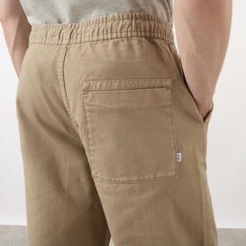 Model wearing Wax London Kurt Drawstring Casual Trousers in khaki, showing back patch pocket and elasticated waistband detail