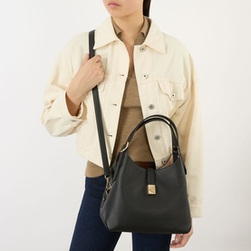 Model carrying Kate Spade Deco Medium Tote Bag in black pebbled leather with gold-tone hardware and crossbody strap, styled with cream jacket and