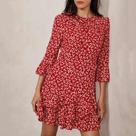 Model wearing Mint Velvet Bow Print Ruffle Mini Dress in red, featuring flared sleeves, ruffle hem, and allover bow print
