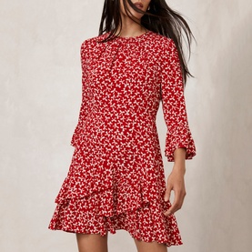 Model wearing Mint Velvet Bow Print Ruffle Mini Dress in red, featuring three-quarter flared sleeves, tiered ruffle hem, and allover ditsy print