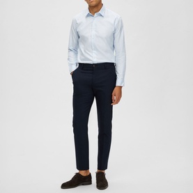 Model wearing Selected Neil Suit Trousers in navy, slim-cut with pressed creases, styled with a light blue shirt and brown suede loafers