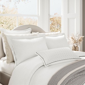 Bedeck Belfast Ayda Square Pillowcase in ivory, styled on a bed with white bedding, grey geometric cushion, and neutral tones throughout