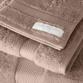 Sheridan Luxury Egyptian Towel in Natural, folded stack of plush blush-toned cotton towels with woven texture detail and branded label