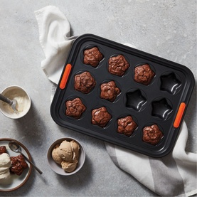 Le Creuset 12-Cup Non-Stick Star Tray 40cm in black with orange handles, filled with star-shaped chocolate brownies, styled with ice cream bowls