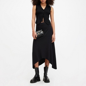 Model wearing All Saints Gia Asymmetric Flared Skirt in black with matching black vest top, styled with chunky black boots and small clutch bag