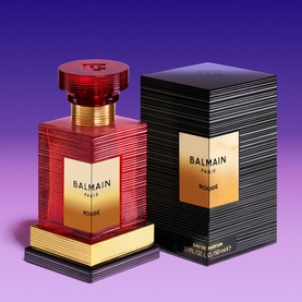 Balmain Rouge Eau de Parfum in red and gold faceted bottle with matching black and gold striped box on purple background.