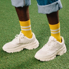 Model with Eat My Socks Soft Gruy&egrave;re Socks in yellow with white stripes, crew style, worn with white chunky trainers and denim shorts