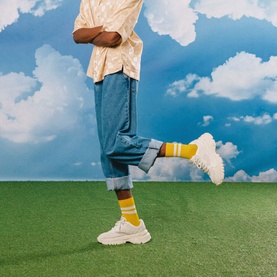 Model with Eat My Socks Soft Gruy&egrave;re Socks in yellow stripe crew style, styled with white chunky trainers and blue denim shorts