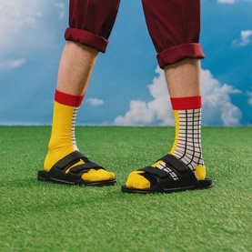 Model with Eat My Socks French Fries Socks in yellow and white check design with red cuff, worn with black slider sandals