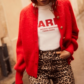 Model wearing Mint Velvet Military Rib Knit Cardigan in red with gold buttons, styled with graphic tee and leopard print trousers