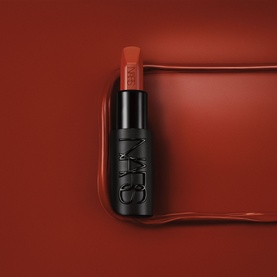 NARS Explicit Lipstick in Incendiary, 4.2g, matte black bullet tube on a deep red sculpted background