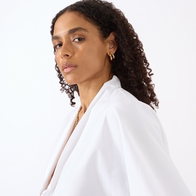 Model with Jenny Bird Florence Earrings in gold-tone, featuring stacked high-polish finish, styled with white blazer and gold chain necklace.