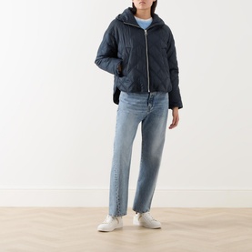 Model wearing Marc O Polo Quilted Cape Jacket in blue with hood, styled with light-wash jeans and white trainers