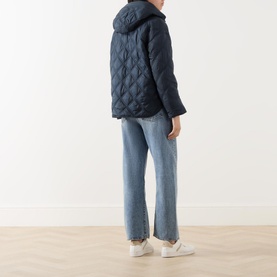 Model wearing Marc O Polo Quilted Cape Jacket in blue, shown from behind, with light-wash straight-leg jeans and white trainers