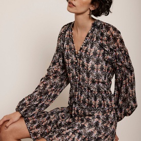 Model wearing Mint Velvet Ruffle-Detail Printed Dress in beige, palm print, V-neckline, long puffed sleeves, front button fastening, mini length