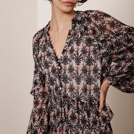 Model wearing Mint Velvet Ruffle-Detail Printed Dress in beige with black floral print, V-neckline and long puffed sleeves with smocked cuffs