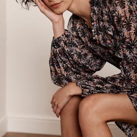 Model wearing Mint Velvet Ruffle-Detail Printed Dress in beige, black floral print, long puffed sleeves with smocked cuffs, mini length