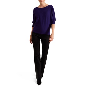 Model wearing Phase Eight Cristine Knitted Sweater in purple with batwing sleeves and slash neckline, styled with black flared trousers and heels