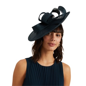Model wearing Phase Eight Bow-Detail Fascinator in blue, wide brim with sculptural bow, set on narrow headband, styled with a pleated blue dress