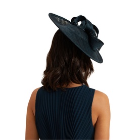 Model wearing Phase Eight Bow-Detail Fascinator in navy blue, wide brim with bow detail, shown from behind with matching blue dress