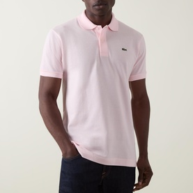 Model wearing Lacoste Heritage Logo Piqu&eacute; Polo Shirt in light pink, with polo collar, two-button placket and crocodile chest logo. Styled with dark