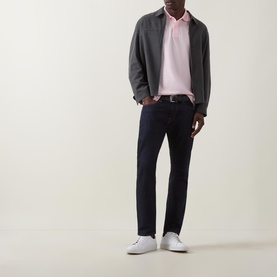 Model wearing Lacoste Heritage Logo Piqu&eacute; Polo Shirt in light pink, styled with grey zip jacket, navy trousers, and white trainers