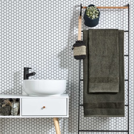 Christys Prism Towel Tarmac in black draped on a ladder rail in a styled bathroom with white hexagonal tile wall and vessel sink