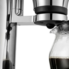 Aarke Coffee Brewer Stainless Steel in silver, close-up showing polished chrome brewer head dispensing dark coffee into glass carafe