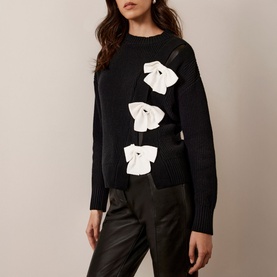 Model wearing Mint Velvet Bow Knit Sweater in black with white bow embellishments, styled with black leather trousers