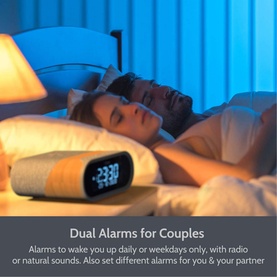 IBox Radio Silver alarm clock on bedside table beside sleeping couple, shown with dual alarm feature text overlay