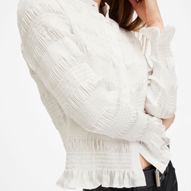 Model wearing All Saints Meg Textured Shirt in white, showing smocked bodice, frill hem, and long sleeves with textured finish