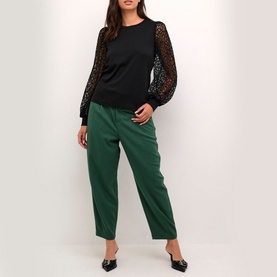 Model wearing Kaffe Becca Lace Top in black with sheer lace sleeves, styled with green tapered trousers and black flat mules
