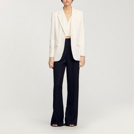 Model wearing Sandro Sequin Suit Blazer in clear, single-breasted, long sleeves, styled with black wide-leg trousers and heels.