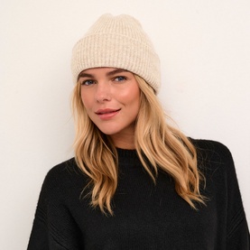 Model wearing Kaffe Marlene Rib Knit Beanie in beige with turned-up brim and rib knit texture, styled with a black knit sweater