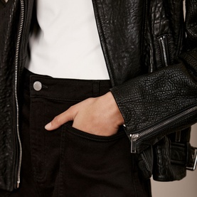 Model wearing Mint Velvet Black Cropped Wide Leg Jeans with hand in pocket, styled with black leather jacket and white top