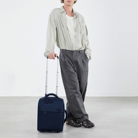 Model carrying Lipault Foldable Plume Mini Cabin Bag 45cm in blue, with extendable handle, styled with grey trousers and sandals