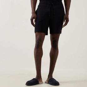 Model wearing Hugo Austin Logo Drawstring Lounge Shorts in black waffle-finish fabric with drawstring waist, styled with dark slip-on slippers.