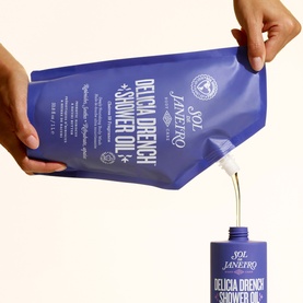 Sol De Janeiro Delicia Drench Shower Oil refill pouch being poured into the pump bottle, shown against a cream background.