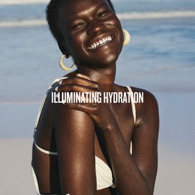 Model with Sol De Janeiro GlowMotions Copacabana Bronze Glow Oil, smiling at beach, skin visibly radiant and luminous