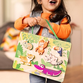 Smiling toddler holding Ravensburger In The Jungle Wooden Touch & Play Puzzle featuring five colourful animal shapes on a green jungle board