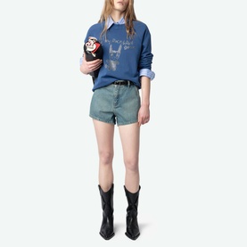 Model wearing Zadig Upper Devil Queen Sweatshirt in blue with rhinestone detailing, styled with denim shorts and black cowboy boots