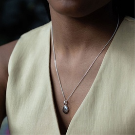 Model with Juvi Small Pebble Pendant Necklace in sterling silver, teardrop pebble pendant on fine snake chain, styled with a yellow vest top