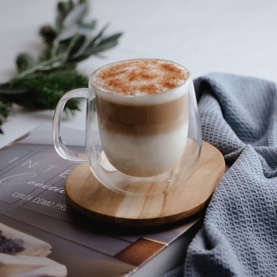 Tramontina Double Walled Glass Coffee Cup with Handle filled with layered latte and cinnamon foam, on wooden coaster