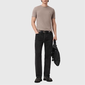 Model wearing All Saints Brace Ramskull Logo T-Shirt in taupe with black jeans and belt, carrying black bag.