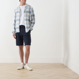 Model wearing Lyle & Scott Eagle Logo Chino Shorts in Dark Navy, styled with a checked overshirt, white tee and white trainers.