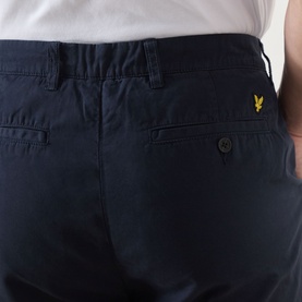 Model wearing Lyle & Scott Eagle Logo Chino Shorts in Dark Navy, close-up of back pocket with gold eagle logo tab detail.