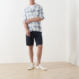 Model wearing Lyle & Scott Eagle Logo Chino Shorts in Dark Navy, styled with a blue check shirt and white trainers.