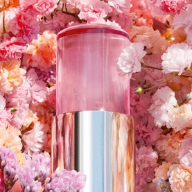 Dior Miss Dior Eau de Parfum Mini Miss Solid Perfume in pink and rose gold casing, displayed against a floral pink blossom background.