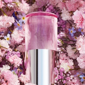 Dior Miss Dior Blooming Bouquet Mini Miss Solid Perfume in pink cylindrical case against floral pink blossom backdrop