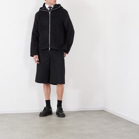 Model wearing Our Legacy Black Zip Through hoodie with white trim, styled with black bermuda shorts and black chunky loafers.